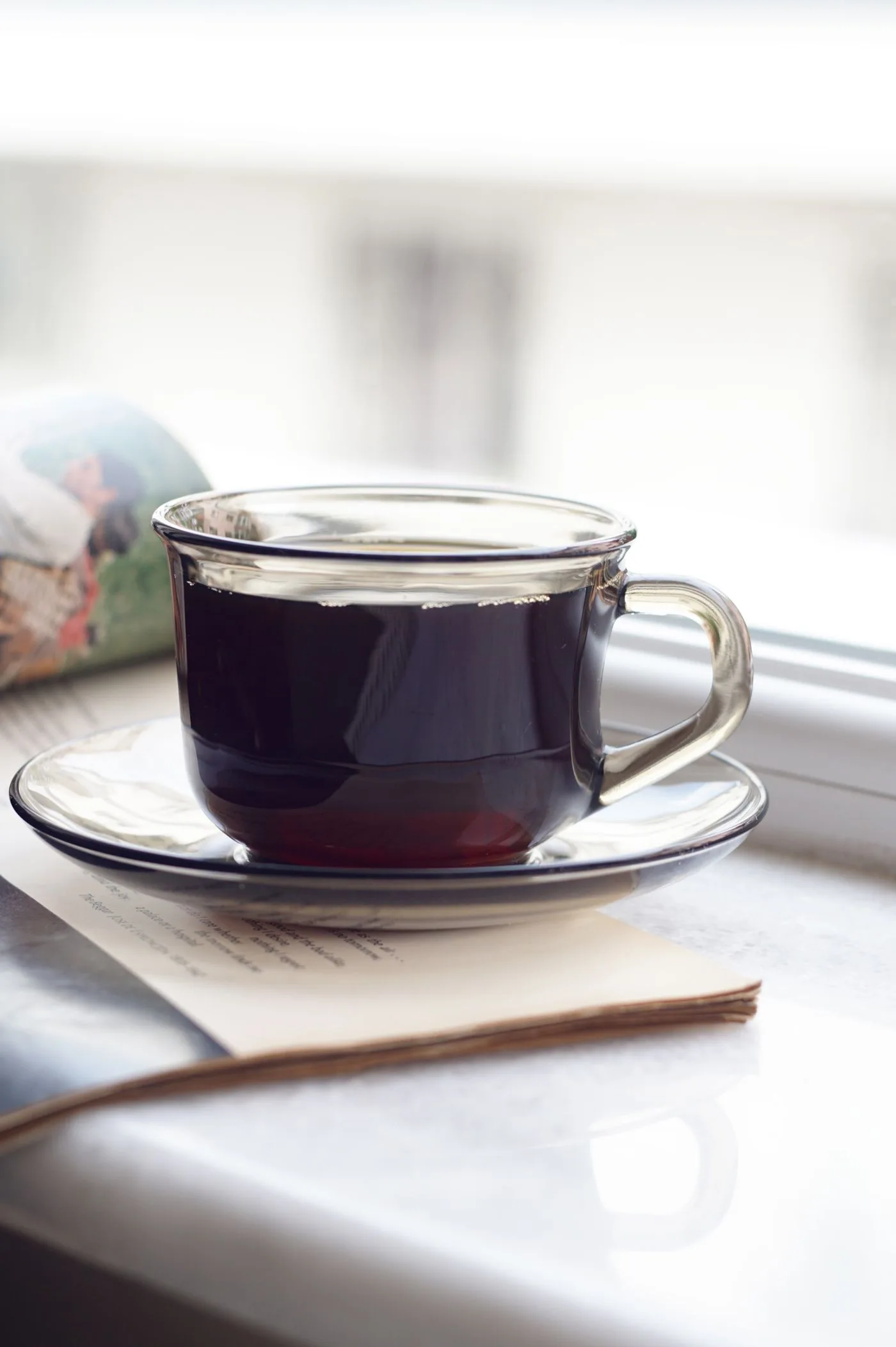 A clear cup of tea and a notebook in soft window light