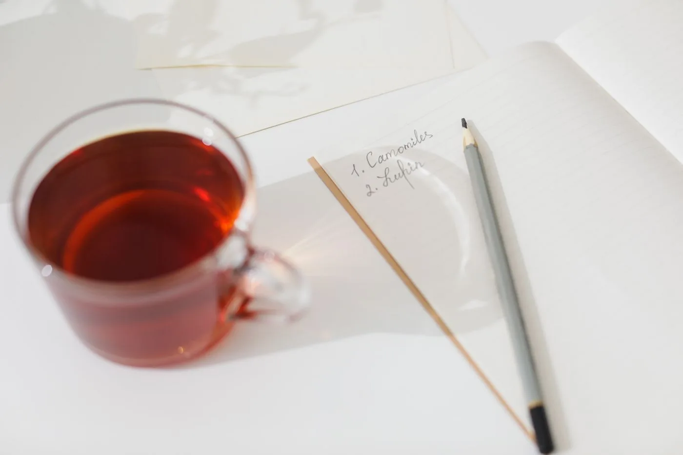 浅色桌面上的一杯茶、摊开的笔记本和铅笔